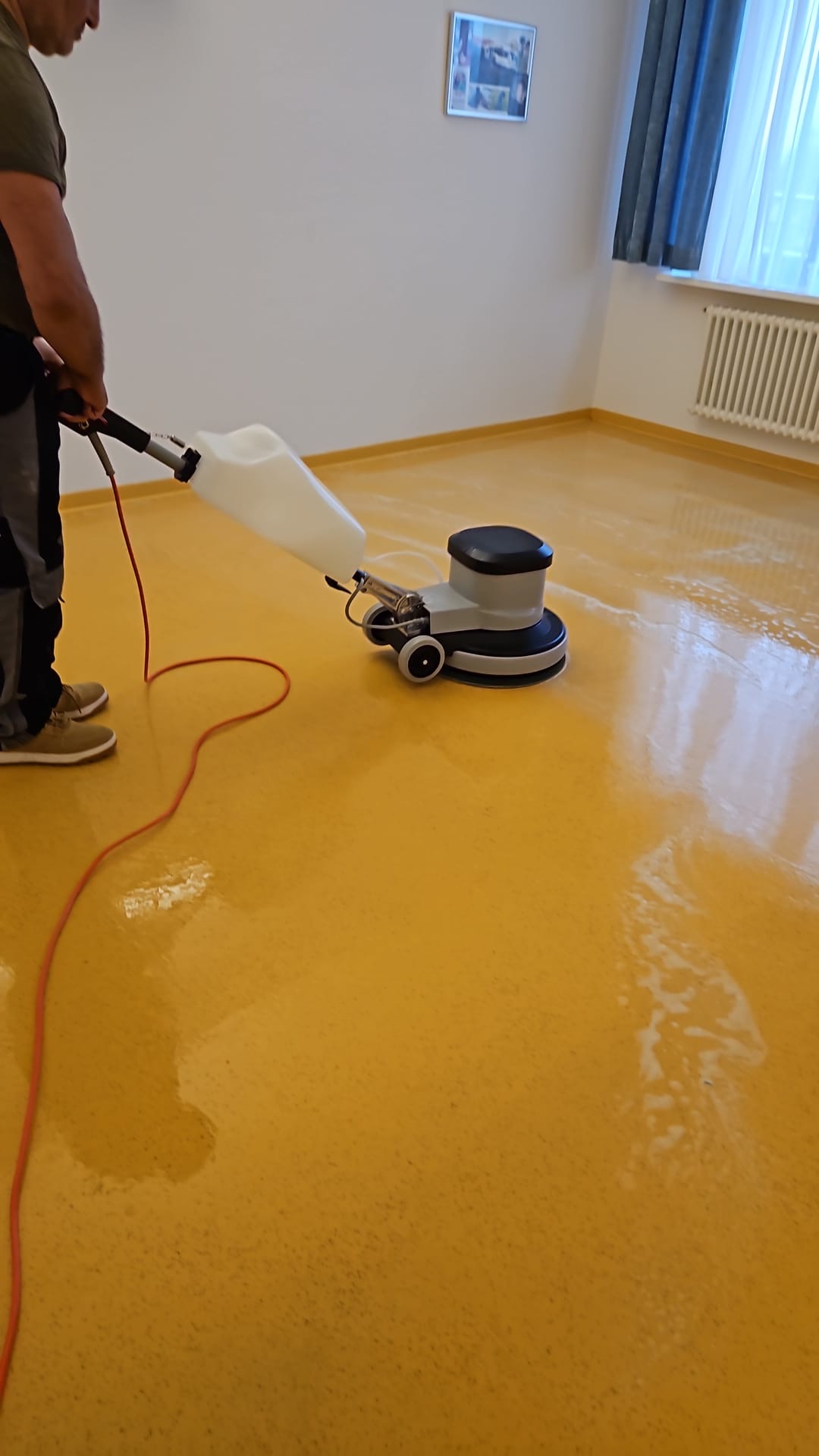 Mitarbeiter reinigt einen Linoleumboden mit einer Einscheibenmaschine