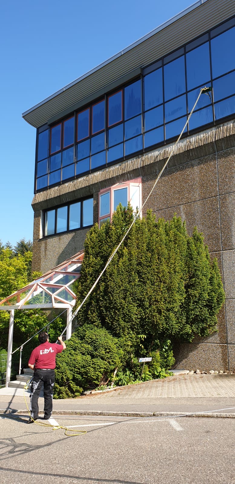Mitarbeiter reinigt eine Glasfassade in Höhe mit einer Teleskopstange