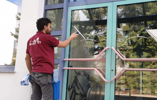 Mitarbeiter reinigt eine Glastür mit Abzieher